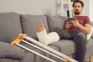 Man sitting on couch with leg on cast and crutches.