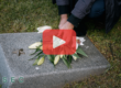 Person putting flowers on grave. Red play button overlay and SEC logo.